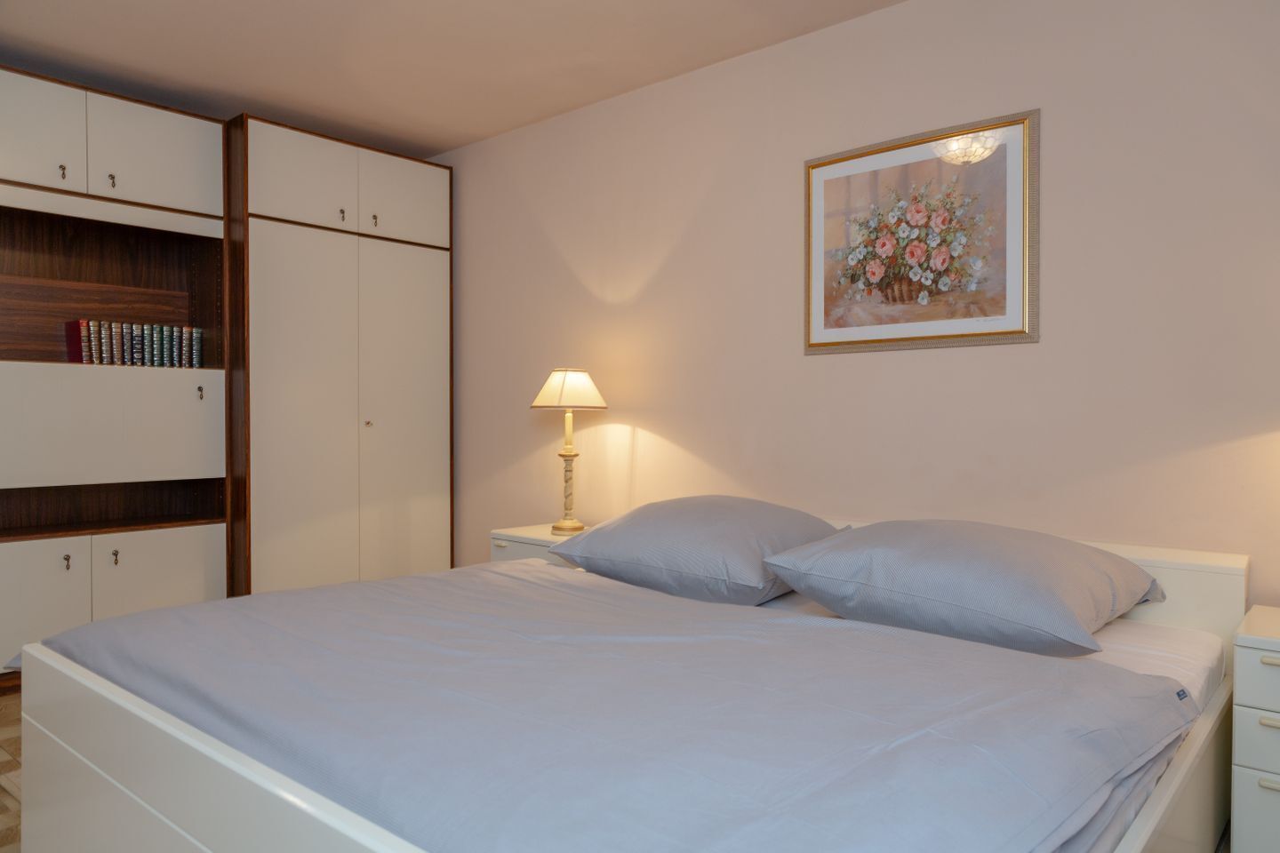 Une chambre à coucher avec un lit, une table de chevet, une lampe, une armoire et un tableau encadré au mur.
