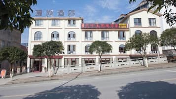 A multi-story hotel with a red signboard, multiple windows, and a tree-lined facade.