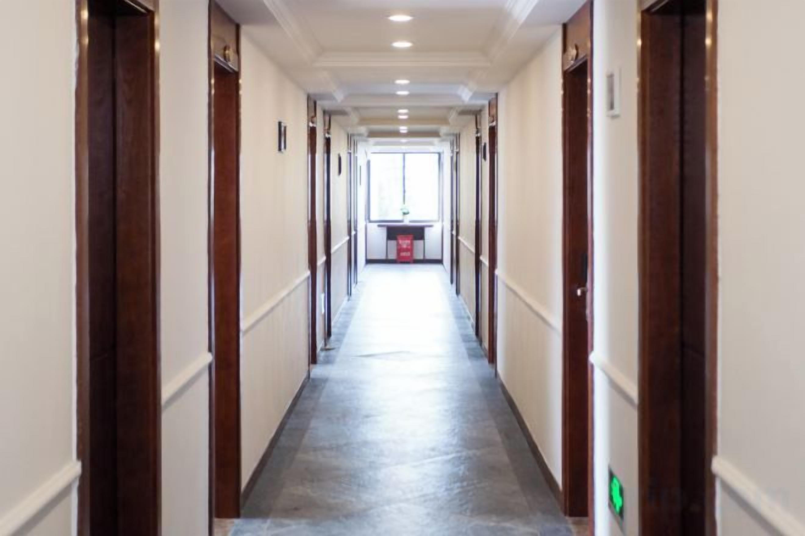 A hotel corridor with doors on both sides, a central walkway, and a window at the end.