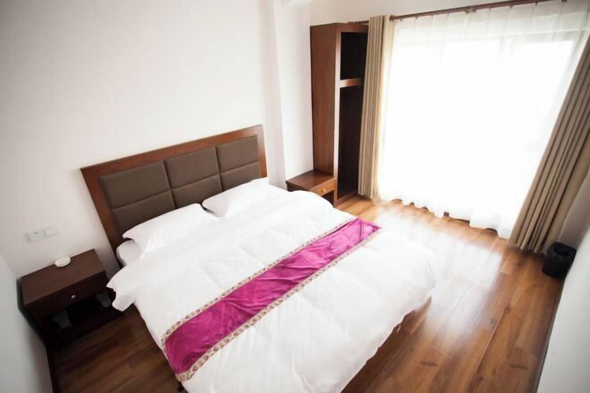 A bedroom with a bed, wooden floor, a nightstand, a wardrobe, and a window with curtains.