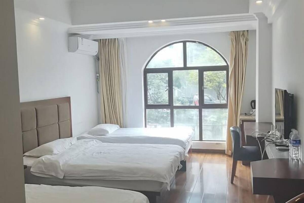 A hotel room with two beds, a desk, and a large arched window with curtains.