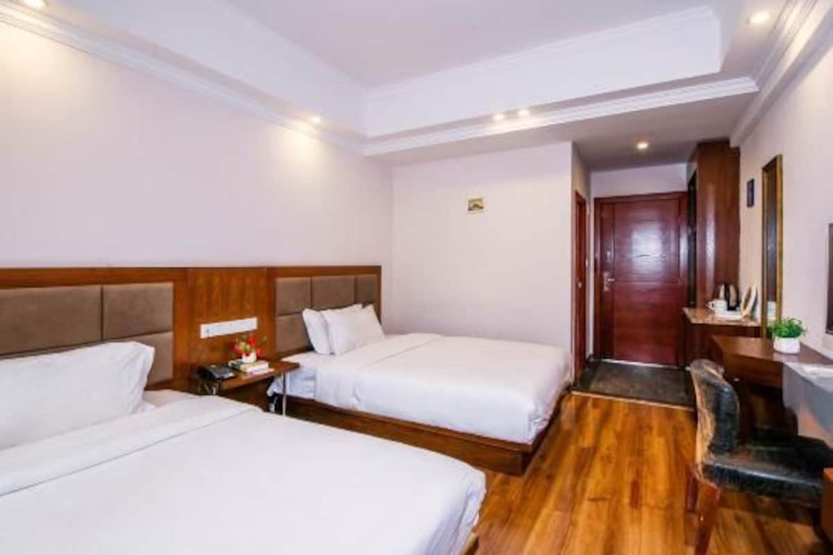 A hotel room with two beds, a desk, a chair, and a wooden floor.