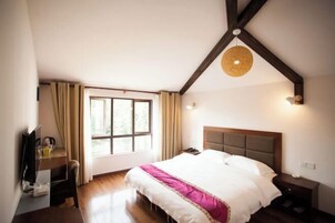 Quarto com uma cama grande, uma escrivaninha, uma cadeira, uma janela com cortinas e um lustre.