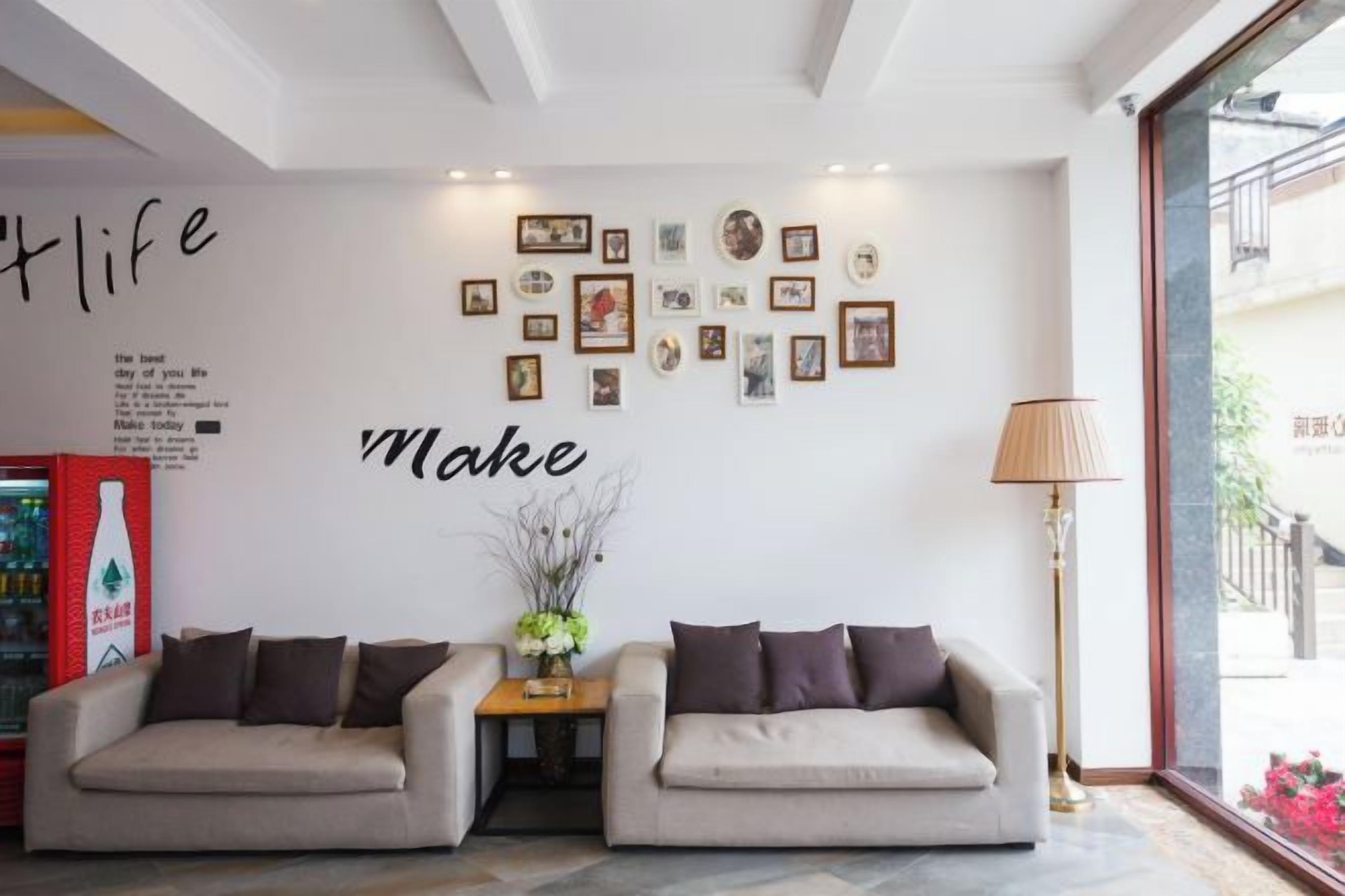A hotel lobby with two sofas, a wall with framed pictures, a lamp, and a bottle of water on a table.