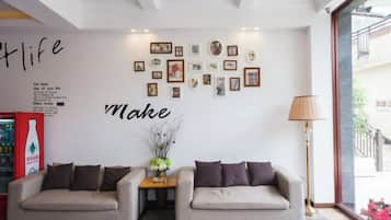 A hotel lobby with two sofas, a wall with framed pictures, a lamp, and a bottle of water on a table.