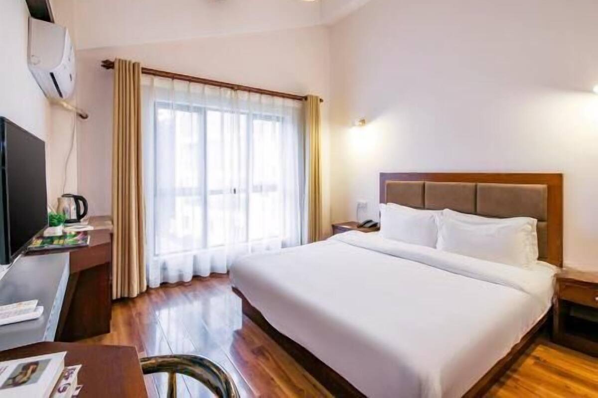 A hotel room with a large bed, a desk with a computer, a coffee maker, and a window with curtains.