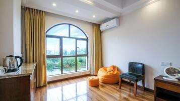 Una habitación con un gran ventanal de arco, suelo de madera, una silla negra, un sillón de bolas naranja y una mesita con una tetera.