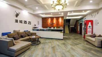 A hotel reception area with a reception desk, sofas, a chandelier, and a staircase in the background.
