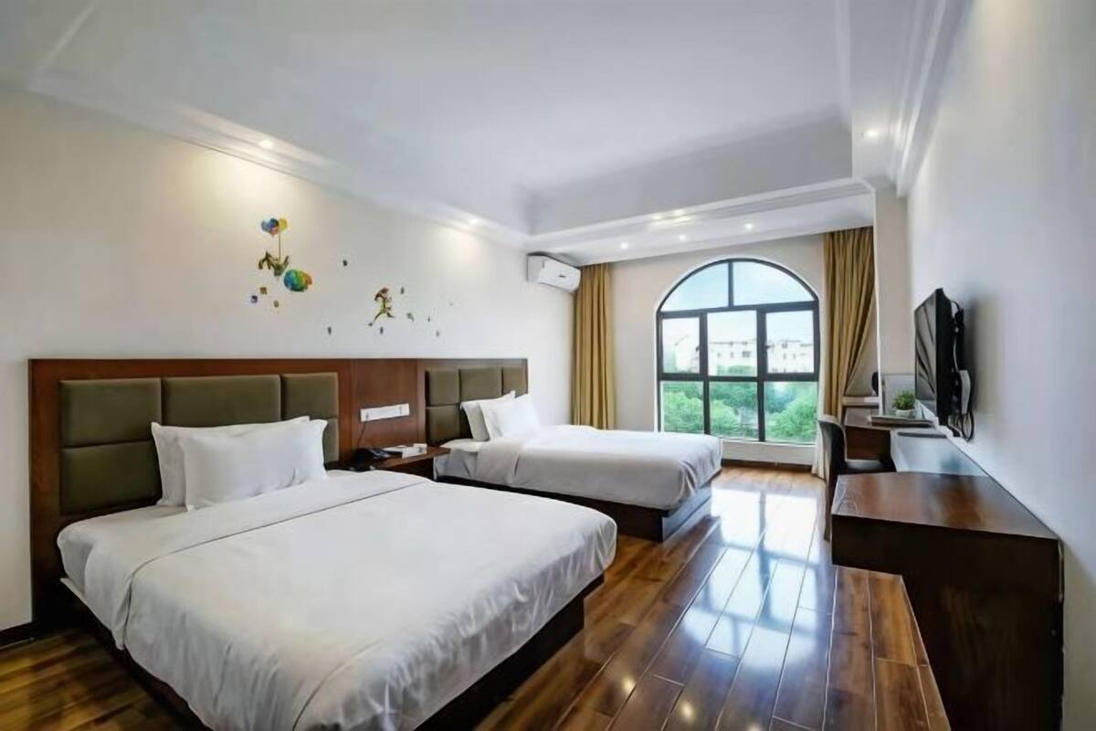 A hotel room with two beds, a desk, a TV, and a large window.