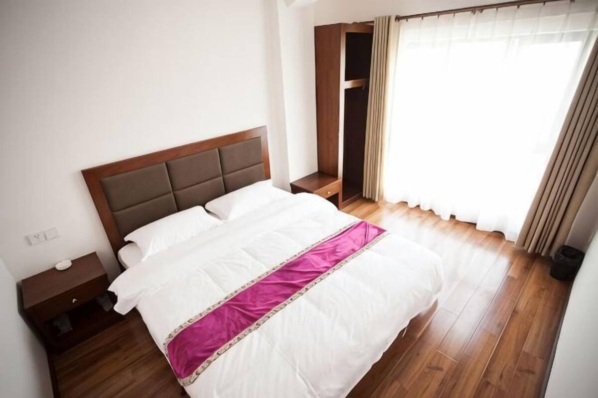 A neatly made bed with a headboard, a bedside table, and a window with curtains.