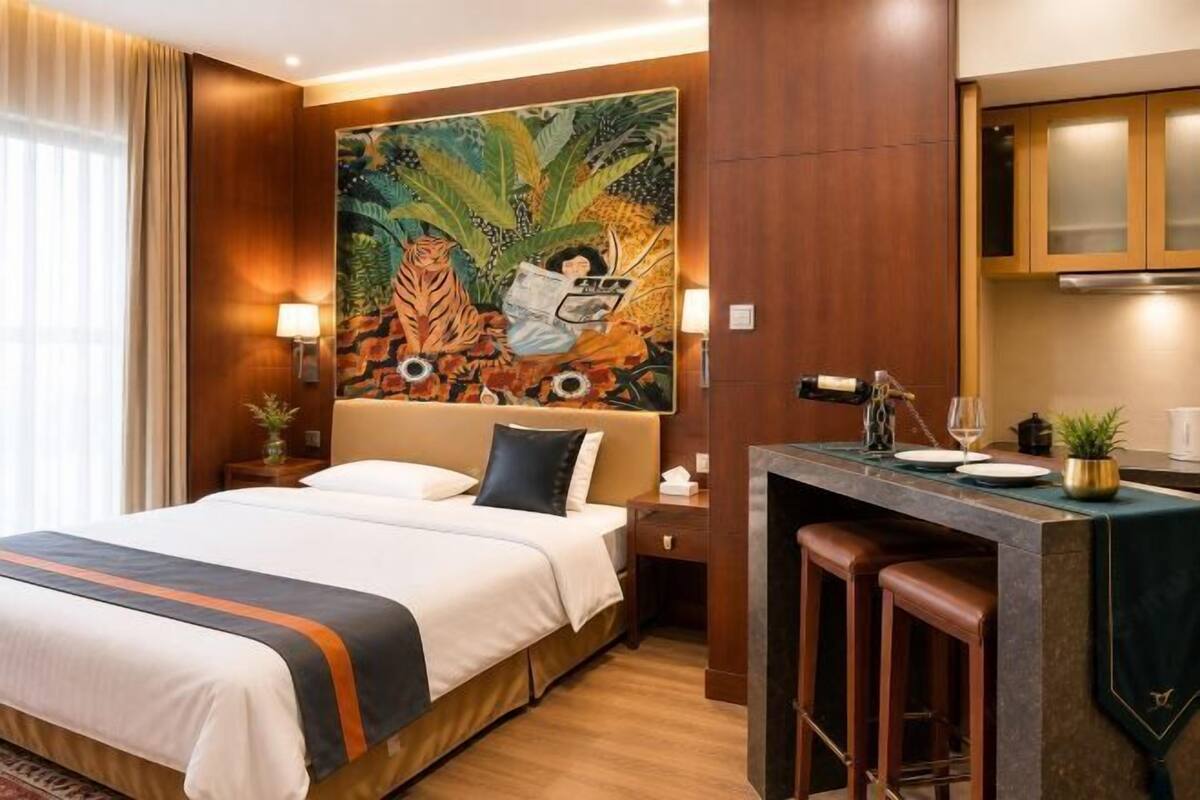 A hotel room with a bed, a painting, a desk, and a bar area.