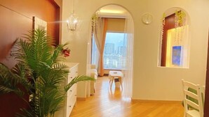 A hallway with wooden flooring, white furniture, a chandelier, and a view of the city through a window. - Ningbo Boteman Apartment (Ningbo)