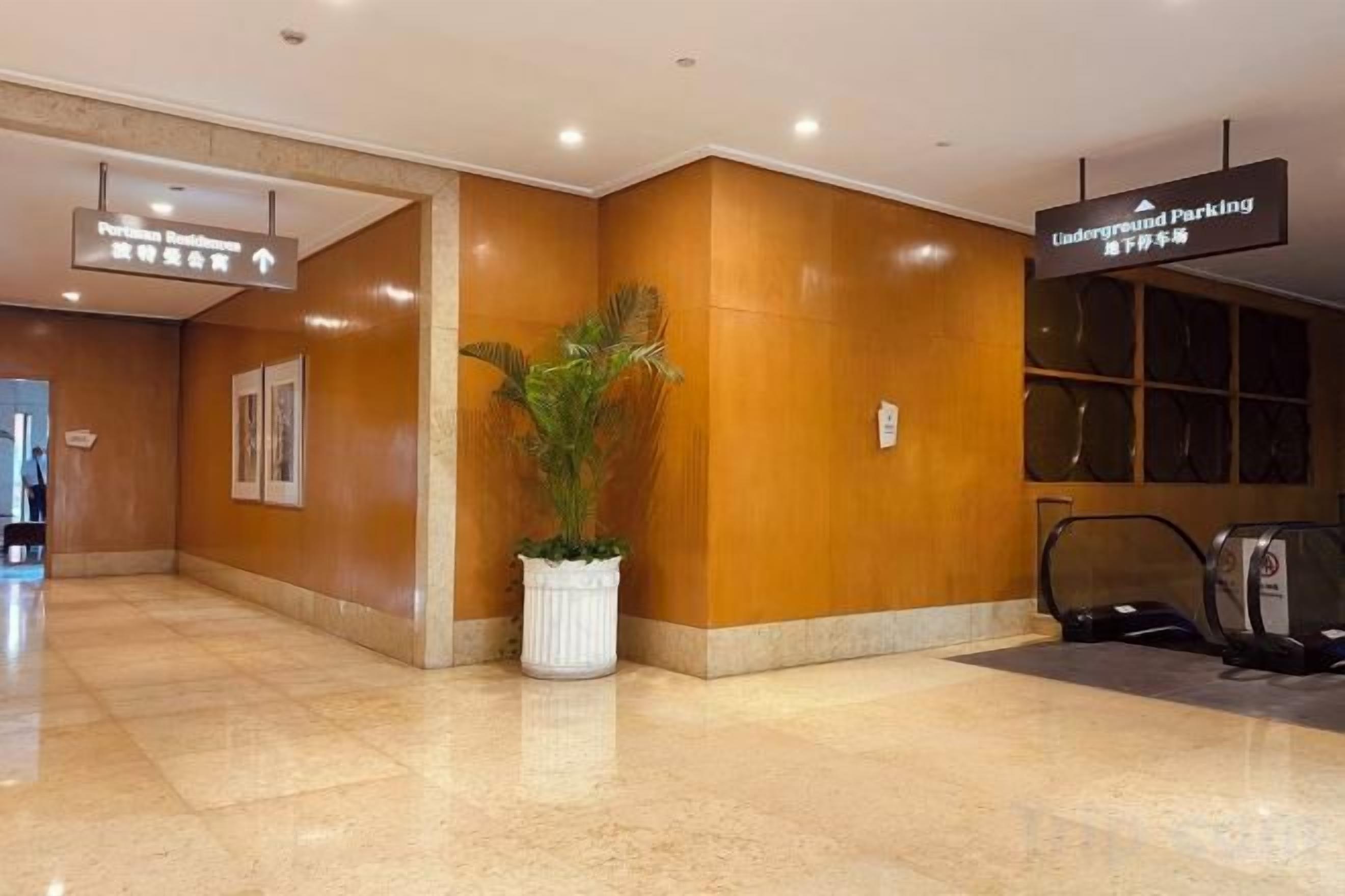 Un hall d’hôtel avec un comptoir d’accueil, une plante en pot et un panneau indiquant l’entrée du parking souterrain.