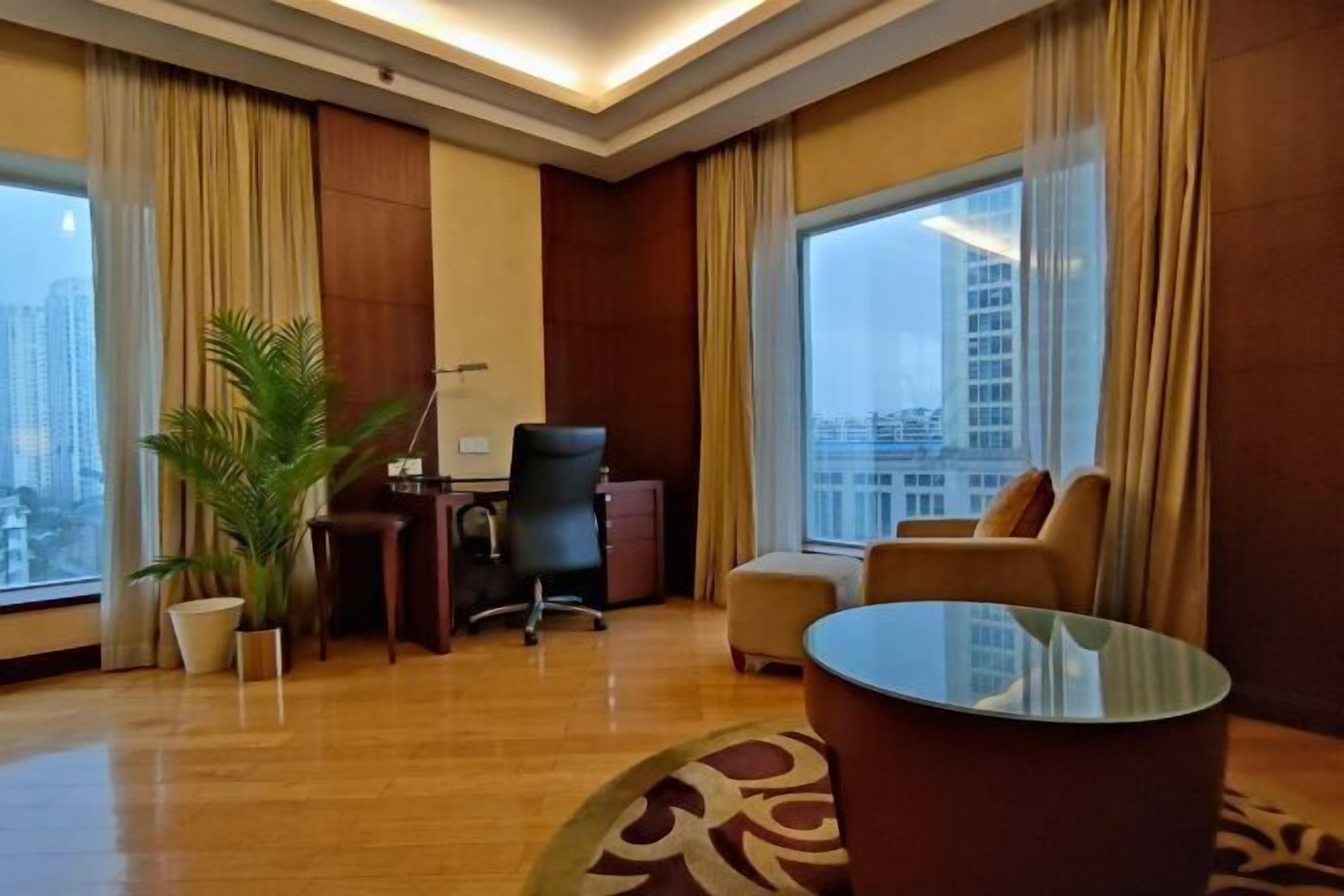 Una habitación de hotel con escritorio, silla de oficina, sofá y una mesa de centro de vidrio.