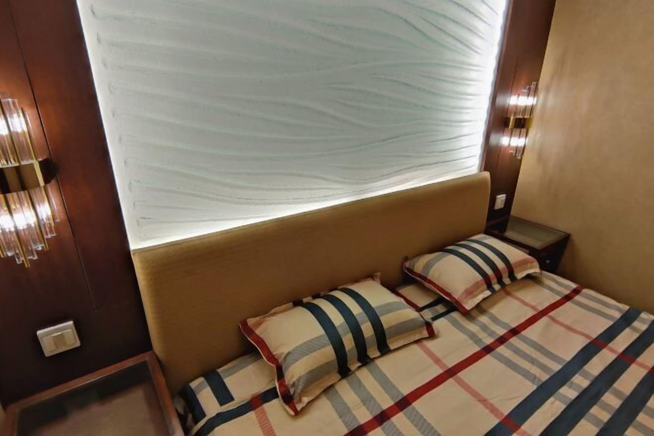 Una habitación de hotel con una cama, dos almohadas, una mesita de noche y una lámpara fijada a la pared.