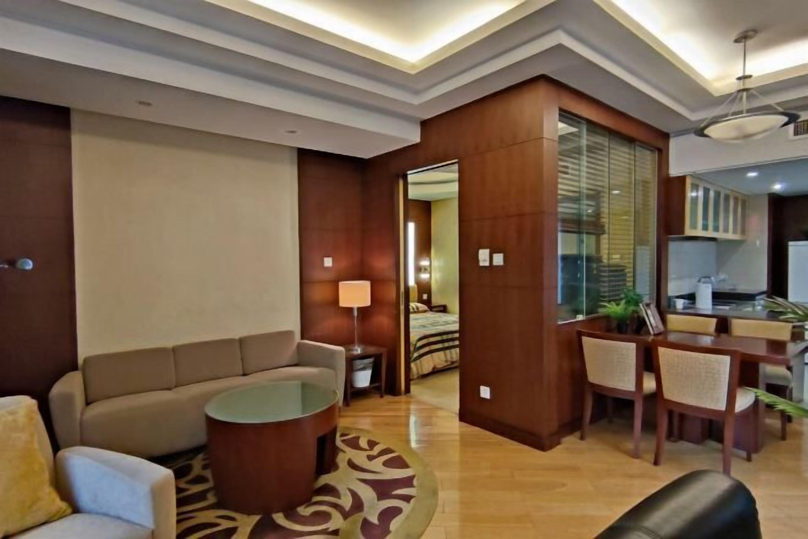 A hotel room with a sofa, a round coffee table, a dining area with a table and chairs, and a kitchen area.