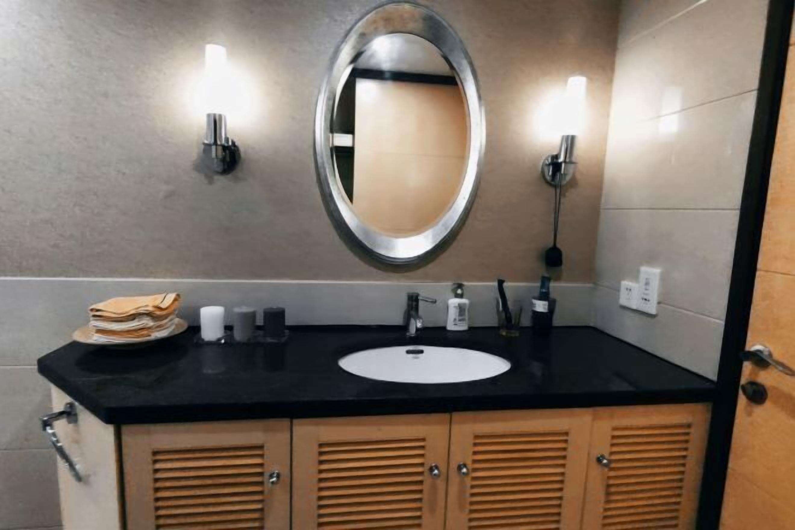 A bathroom with a black countertop, a white sink, a mirror, and wooden cabinets.