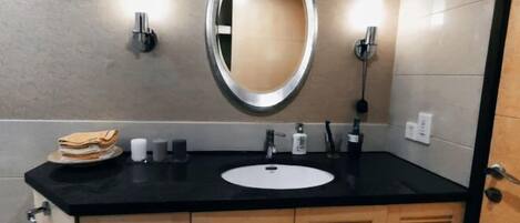 A bathroom with a black countertop, a white sink, a mirror, and wooden cabinets.