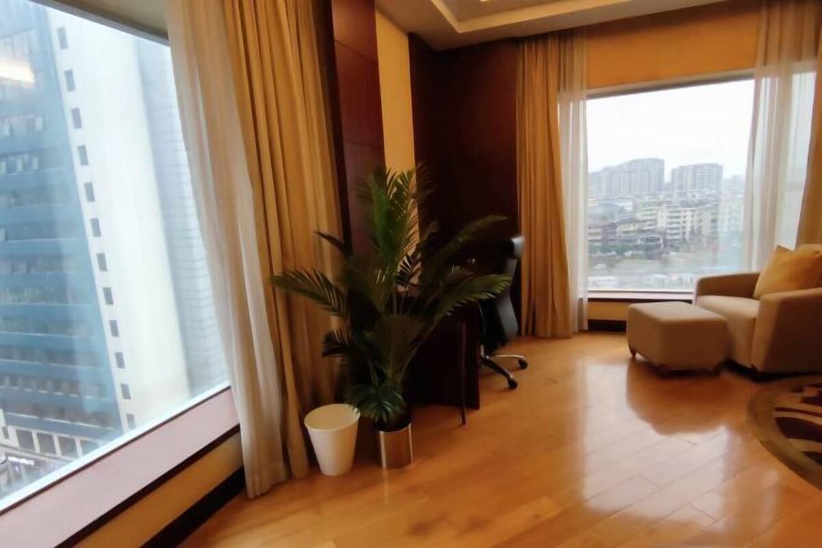 A modern hotel room with a large window, a potted plant, a sofa, and a desk.