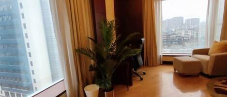 Une chambre d’hôtel moderne avec une grande fenêtre, une plante en pot, un canapé et un bureau.