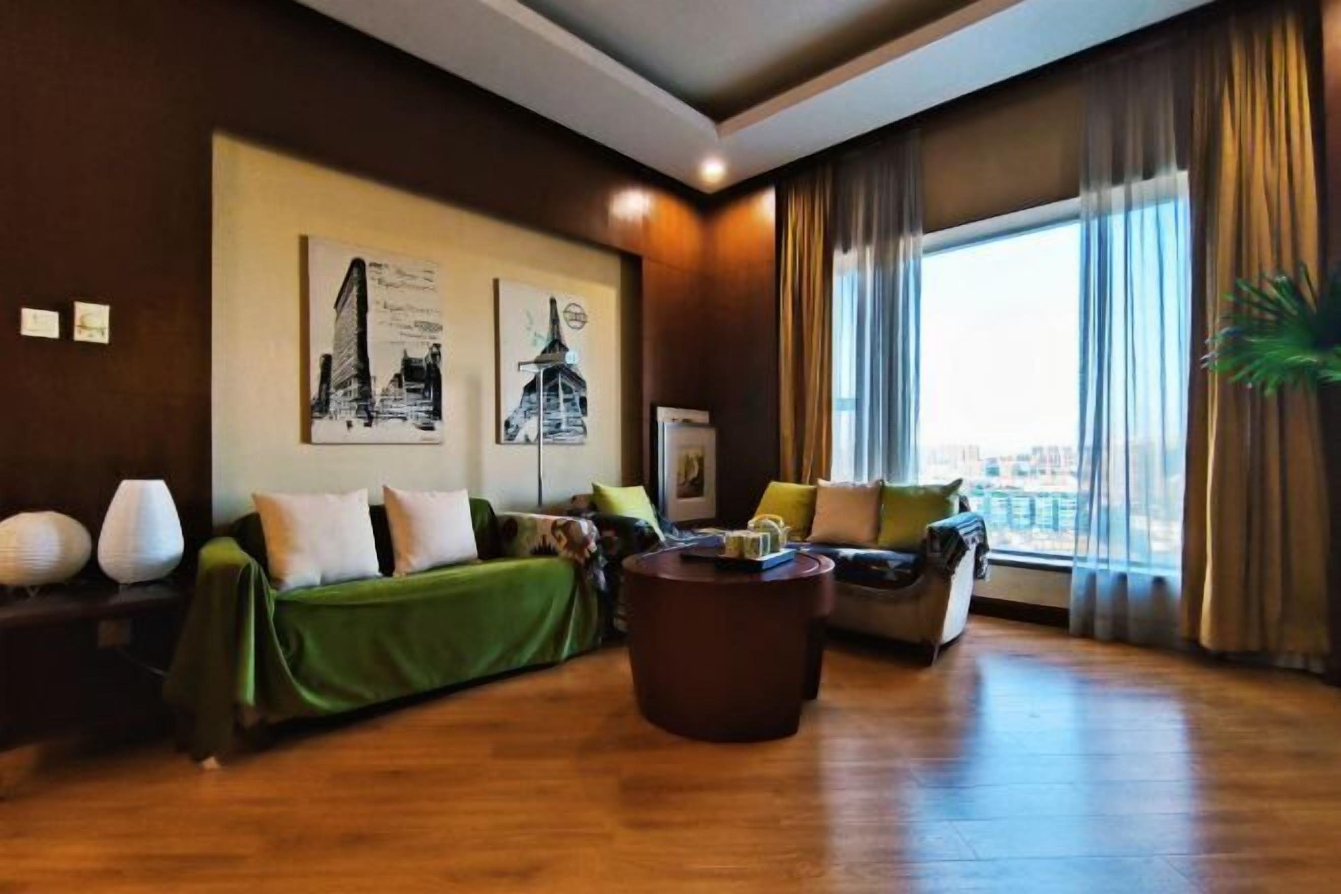 A modern living room with a green sofa, a brown coffee table, and a large window with curtains.