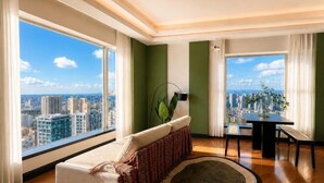 A modern living room with a sofa, a dining table, and a view of a cityscape through large windows. - Ningbo Boteman Apartment (Ningbo)