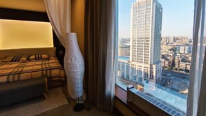 A hotel room with a bed, a bedside table, a window with a city view, and a curtain. - Ningbo Boteman Apartment (Ningbo)