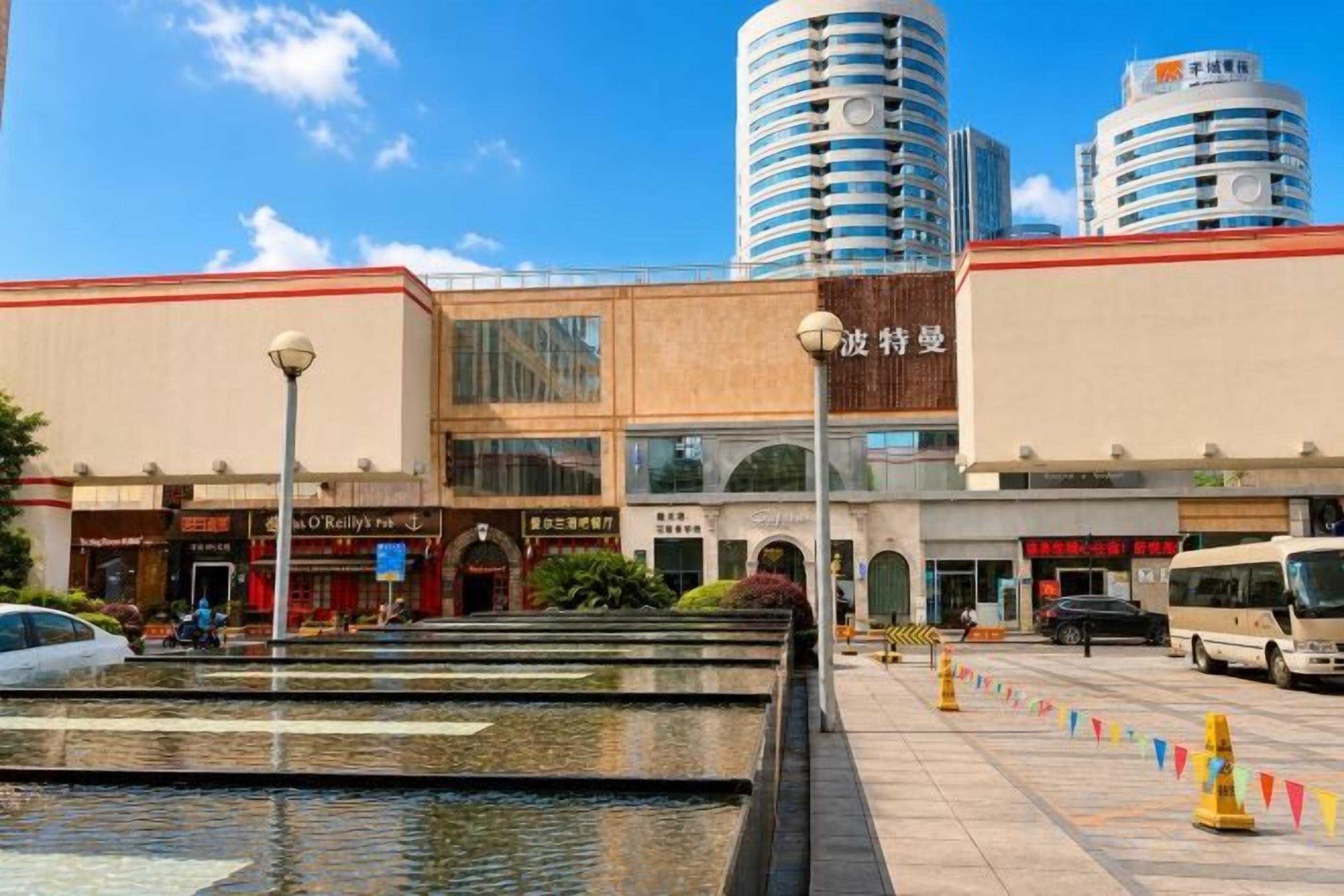 A commercial building with a fountain, a parking lot, and a bus.