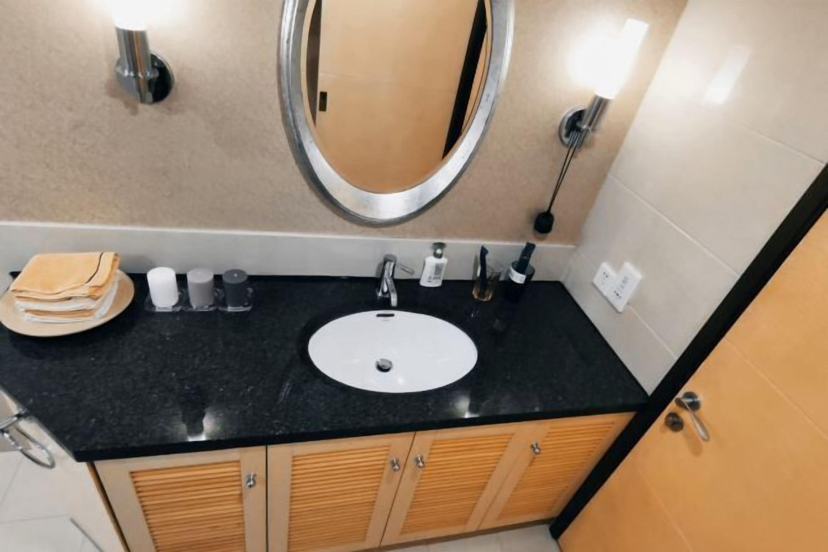 Un baño con encimera negra, lavabo blanco, espejo y armarios de madera.