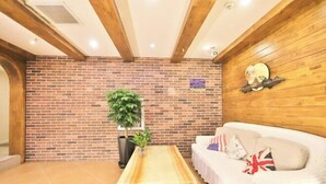 Een kamer met een bakstenen muur, houten balken in het plafond, een witte bank met kussens en een houten salontafel.