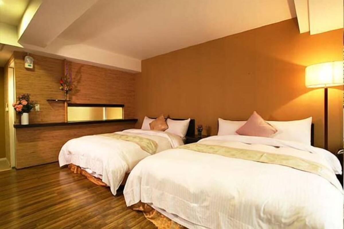 Une chambre d’hôtel avec deux lits, un plancher en bois, un mur décoratif en bois et une table de chevet avec une lampe.