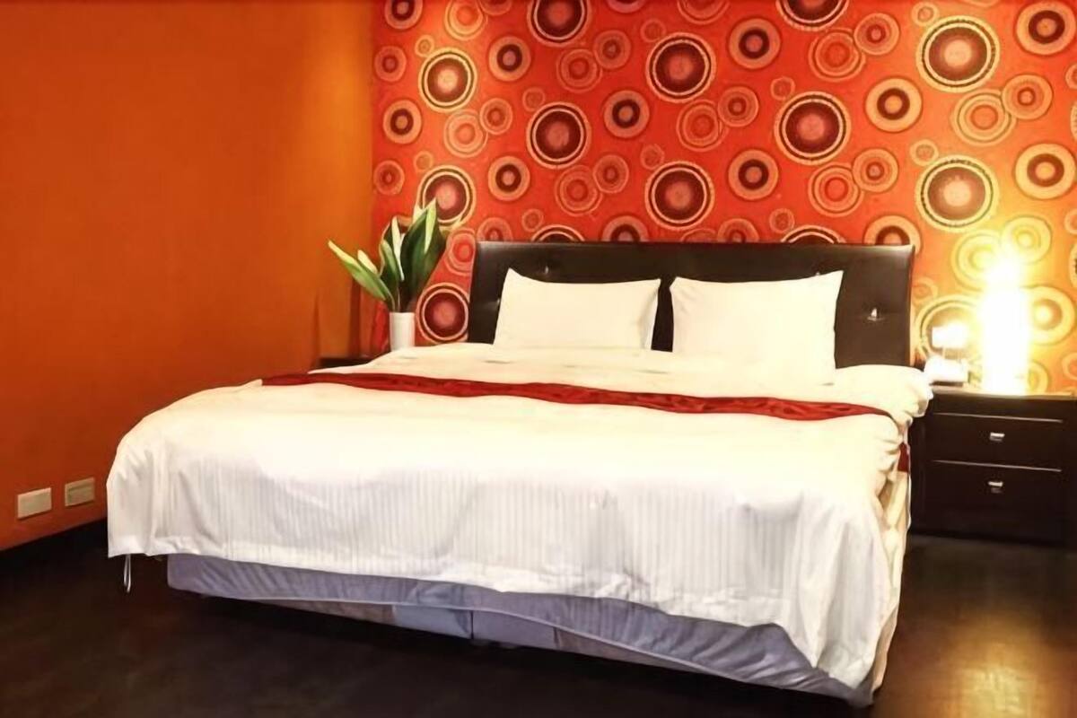 Un lit avec une couvre-lit blanche, une tête de lit sombre et une table de chevet avec une lampe.