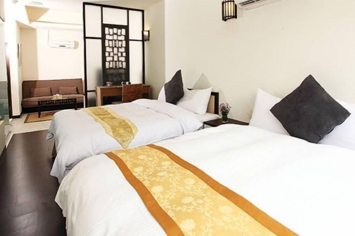Une chambre d’hôtel avec deux lits, un canapé, une petite table et un paravent décoratif.
