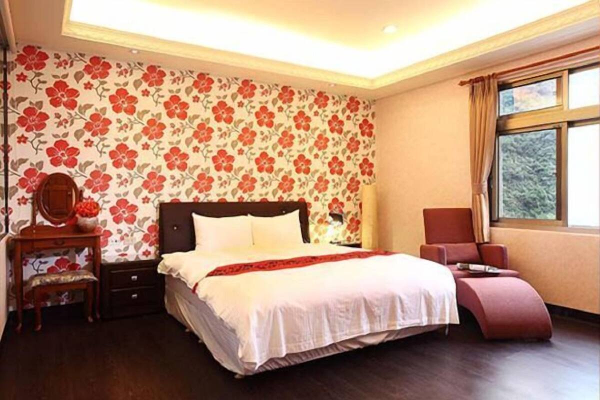 Une chambre à coucher avec un grand lit, une table de chevet, une commode, une chaise et une fenêtre avec des rideaux.