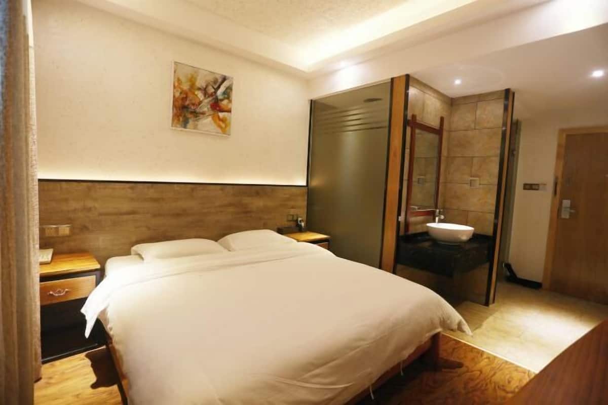 A hotel room with a bed, a nightstand, a painting on the wall, and a bathroom with a sink and mirror.