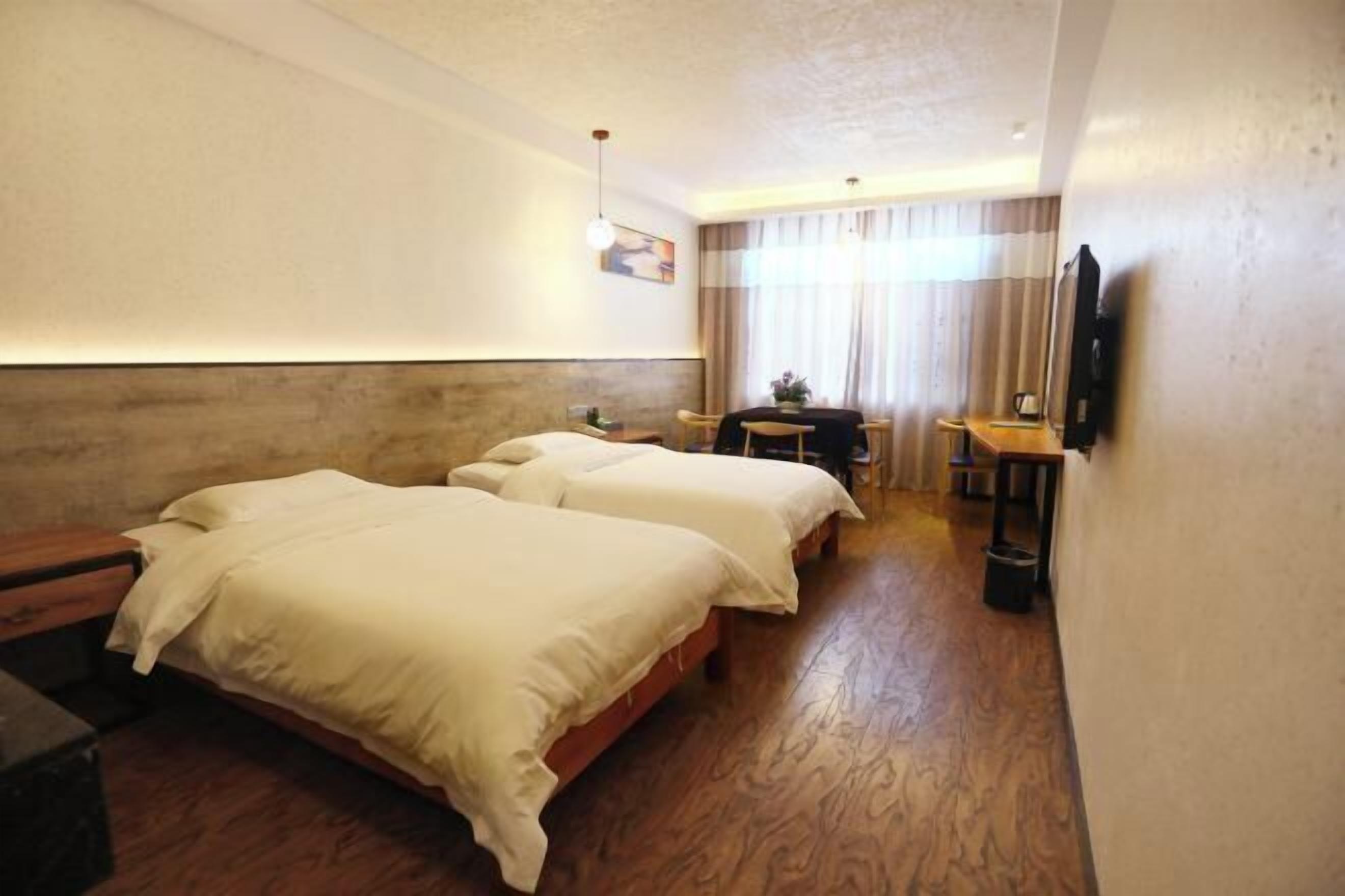 A hotel room with two beds, a desk, a chair, a television, and a window with curtains.