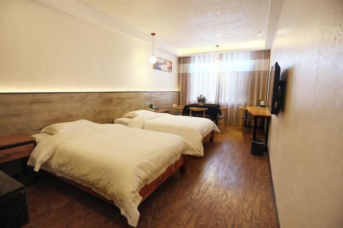A hotel room with two beds, a small table, a chair, a TV, and a window with curtains.