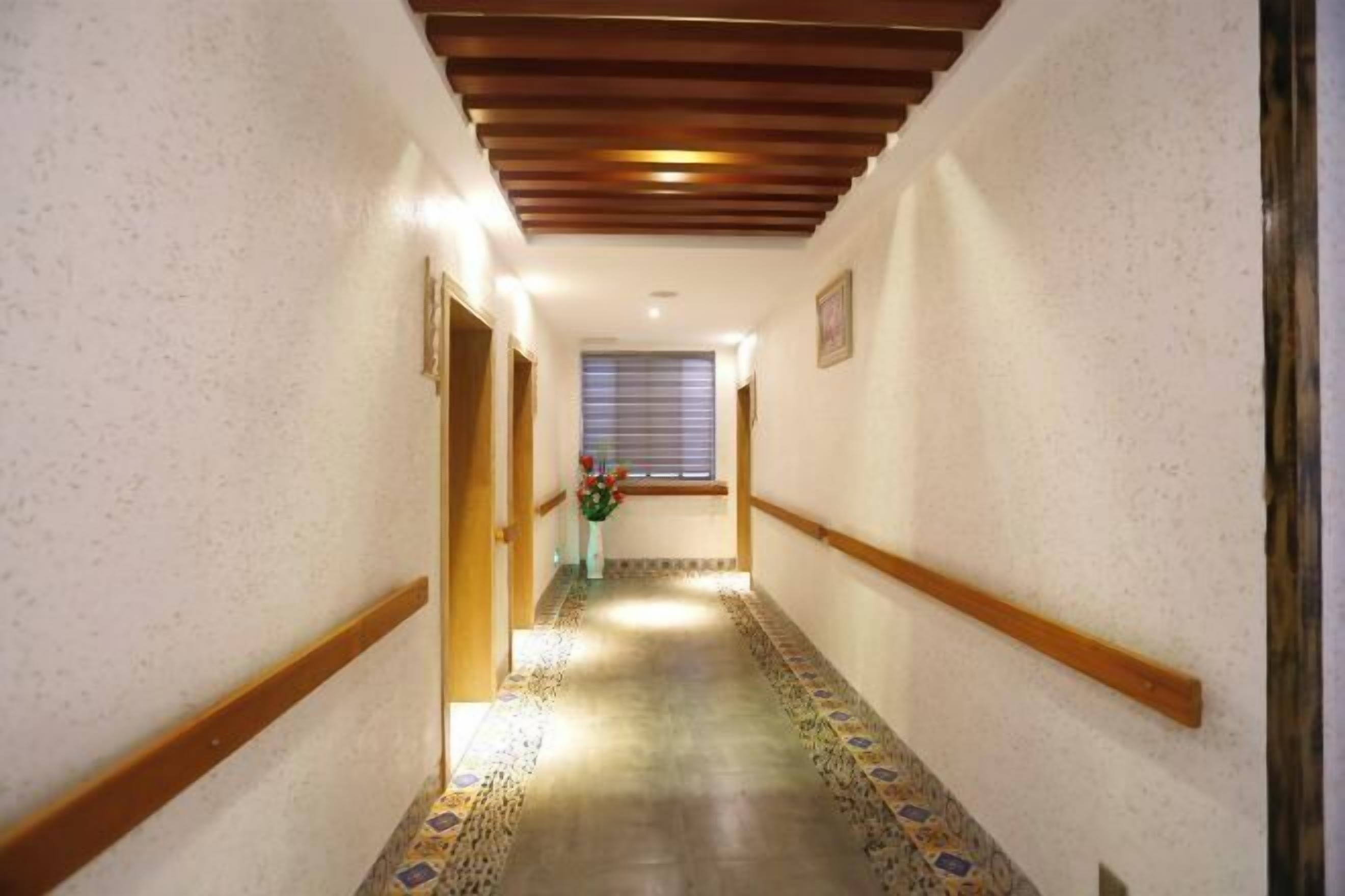 A hallway with a patterned floor, wooden beams on the ceiling, and a window with blinds.