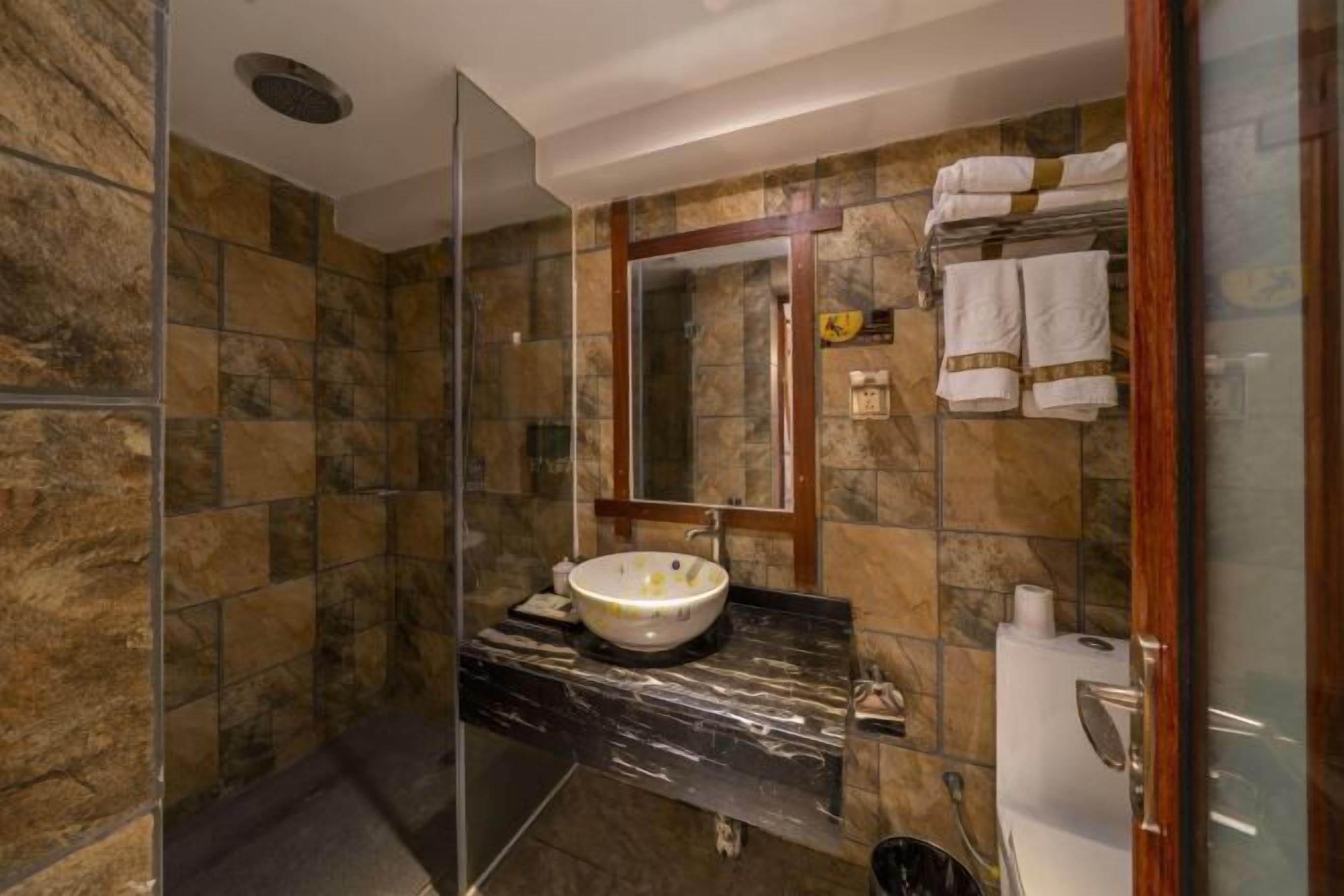 Une salle de bain avec un mur en pierre, un comptoir en marbre, un lavabo avec un miroir et une cabine de douche en verre.