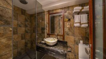 Une salle de bain avec un mur en pierre, un comptoir en marbre, un lavabo avec un miroir et une cabine de douche en verre.