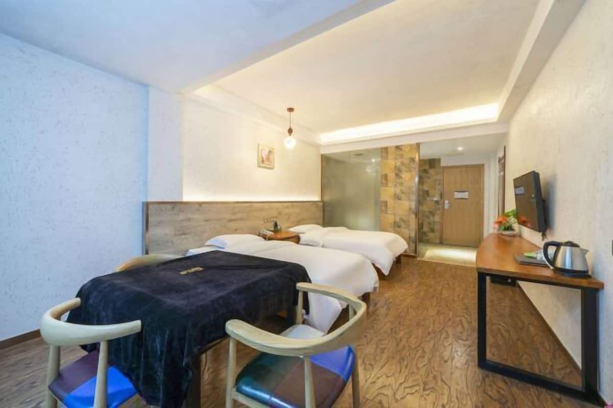 A hotel room with two beds, a desk with a kettle, a chair, and a television.