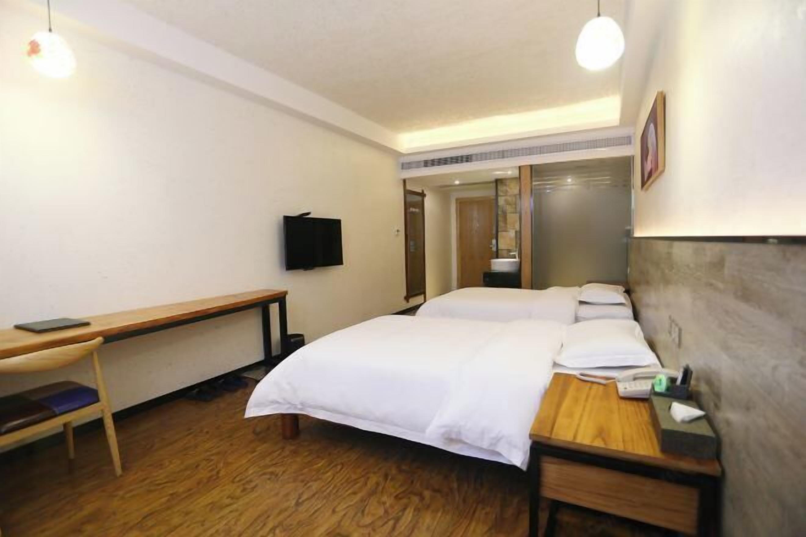 A hotel room with a bed, bedside table, desk, chair, television, and a mirror.