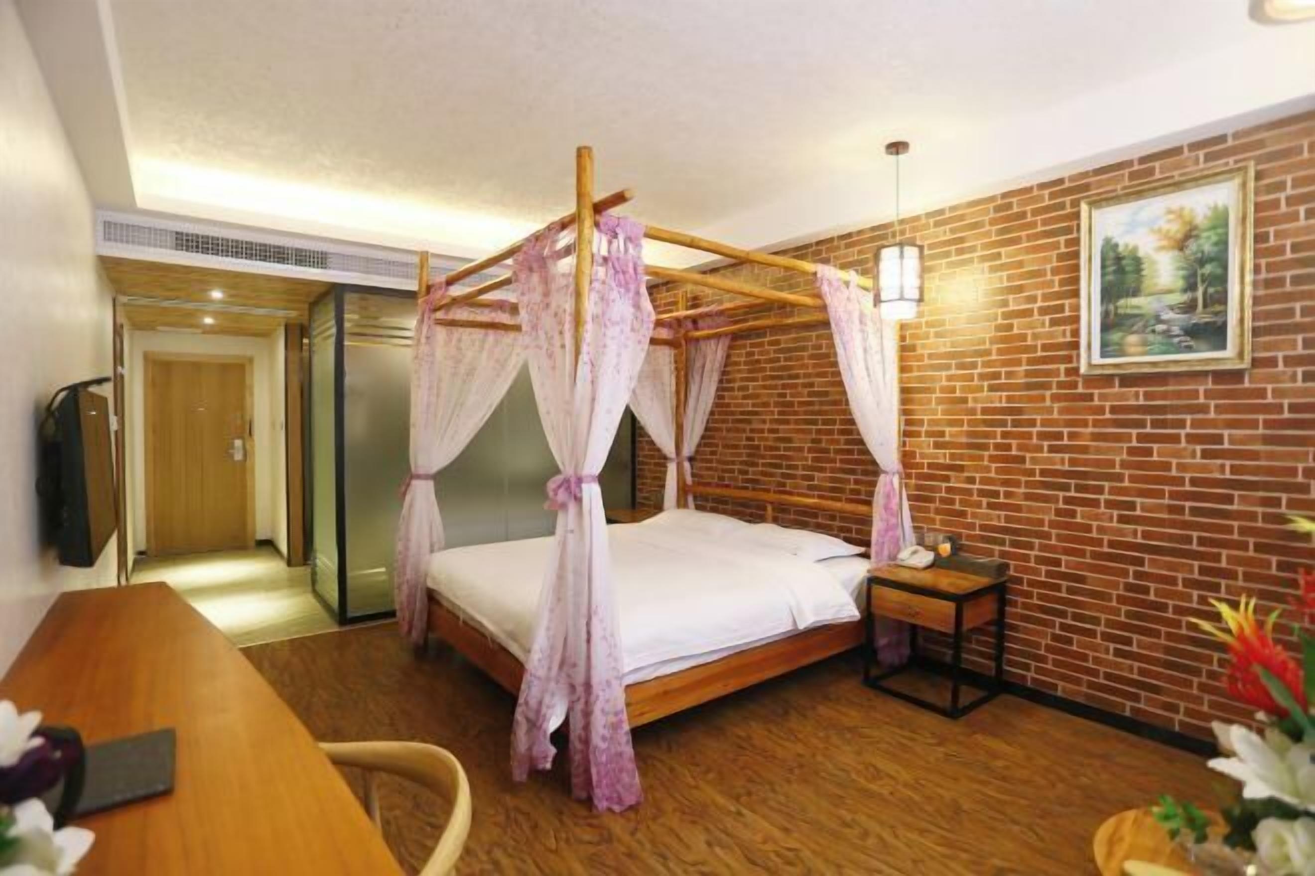 Un dormitorio con una cama con dosel, un escritorio de madera, una mesita de noche y una pared de ladrillo.