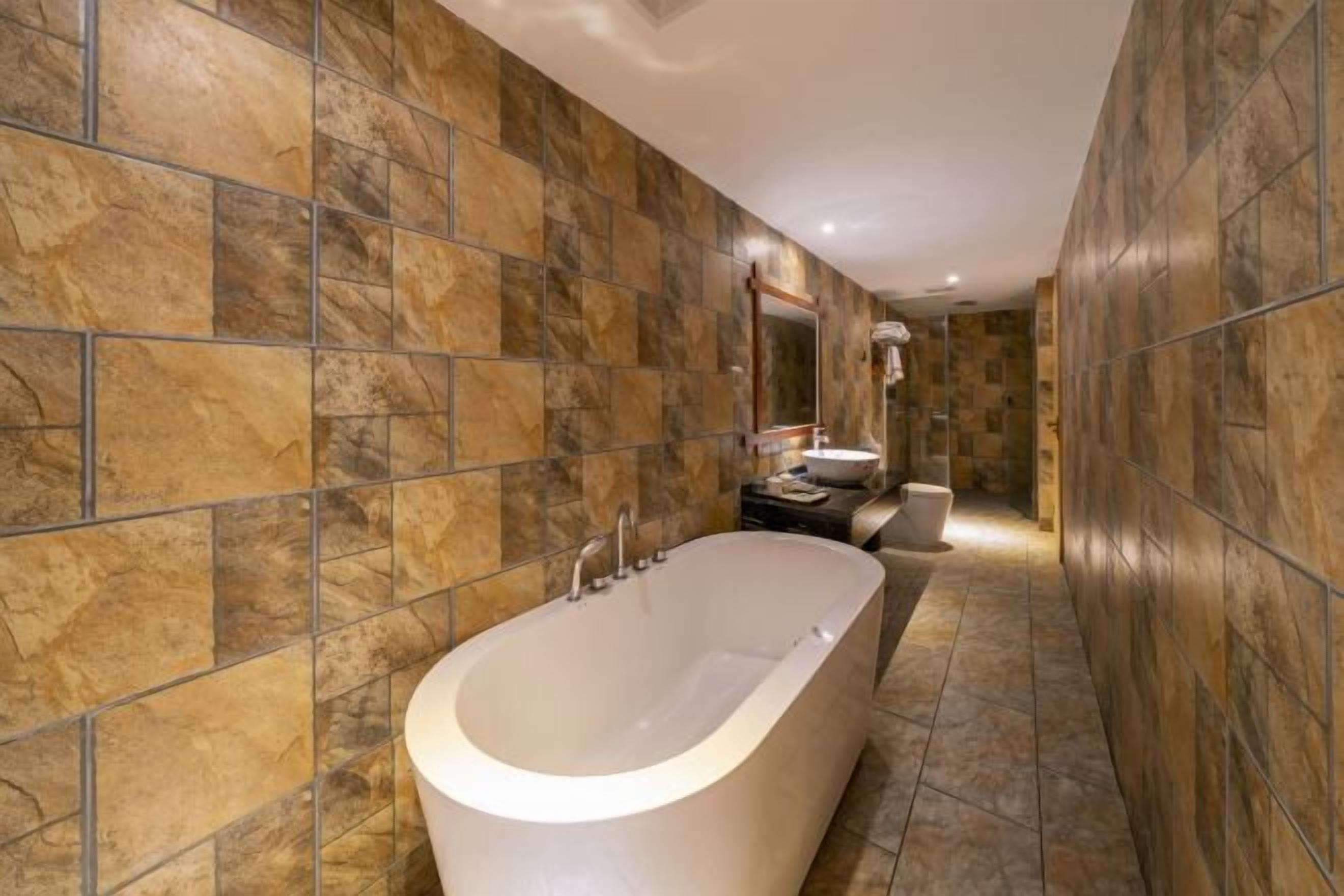 Un baño moderno con bañera independiente, paredes con azulejos y un espejo sobre el lavamanos.