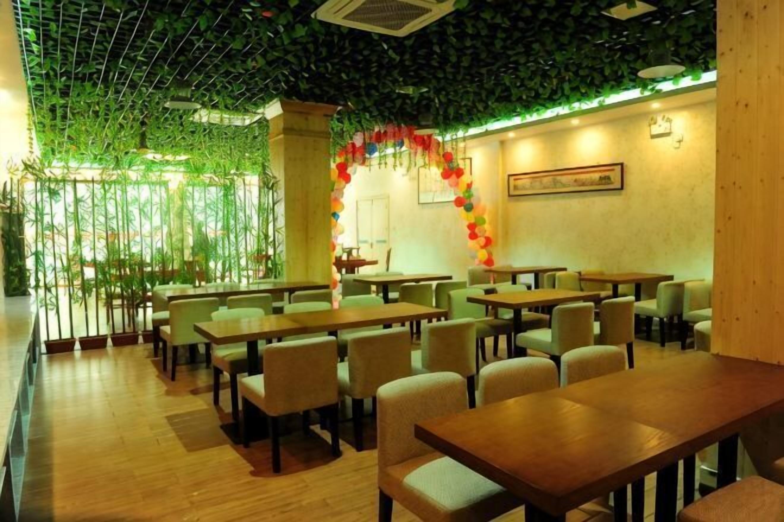 Un restaurant avec des tables et des chaises en bois, un plafond verdoyant orné de feuillages et une arche décorative.