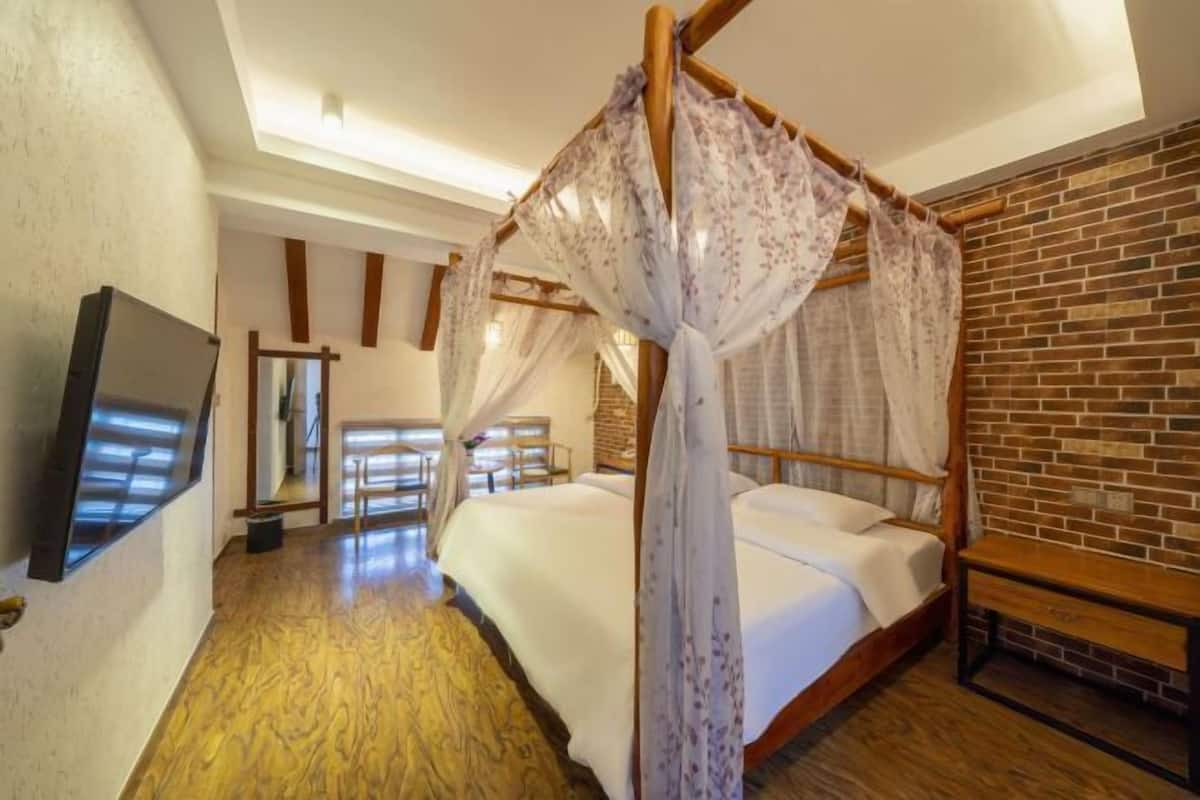 A room with a four-poster bed, a television mounted on the wall, and a brick wall.