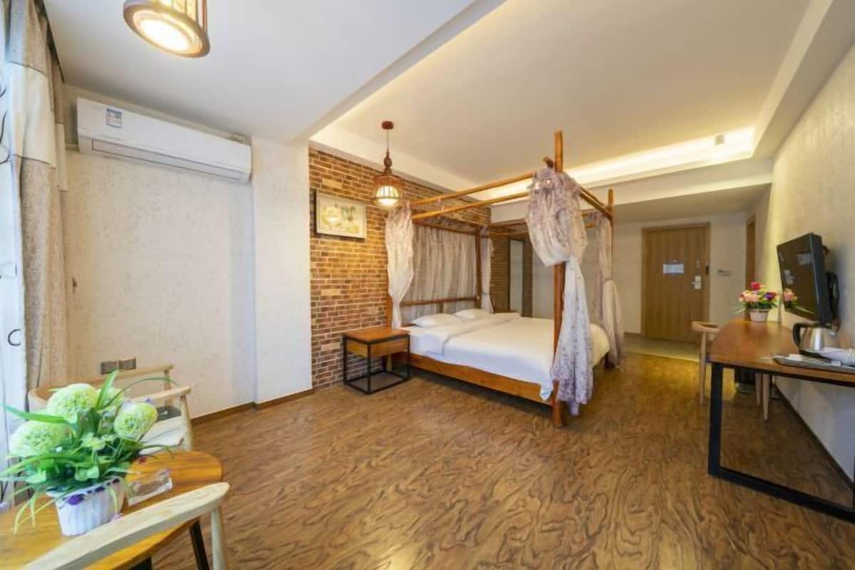 A room with a four-poster bed, a small table with a plant, a TV on a stand, and a brick wall.