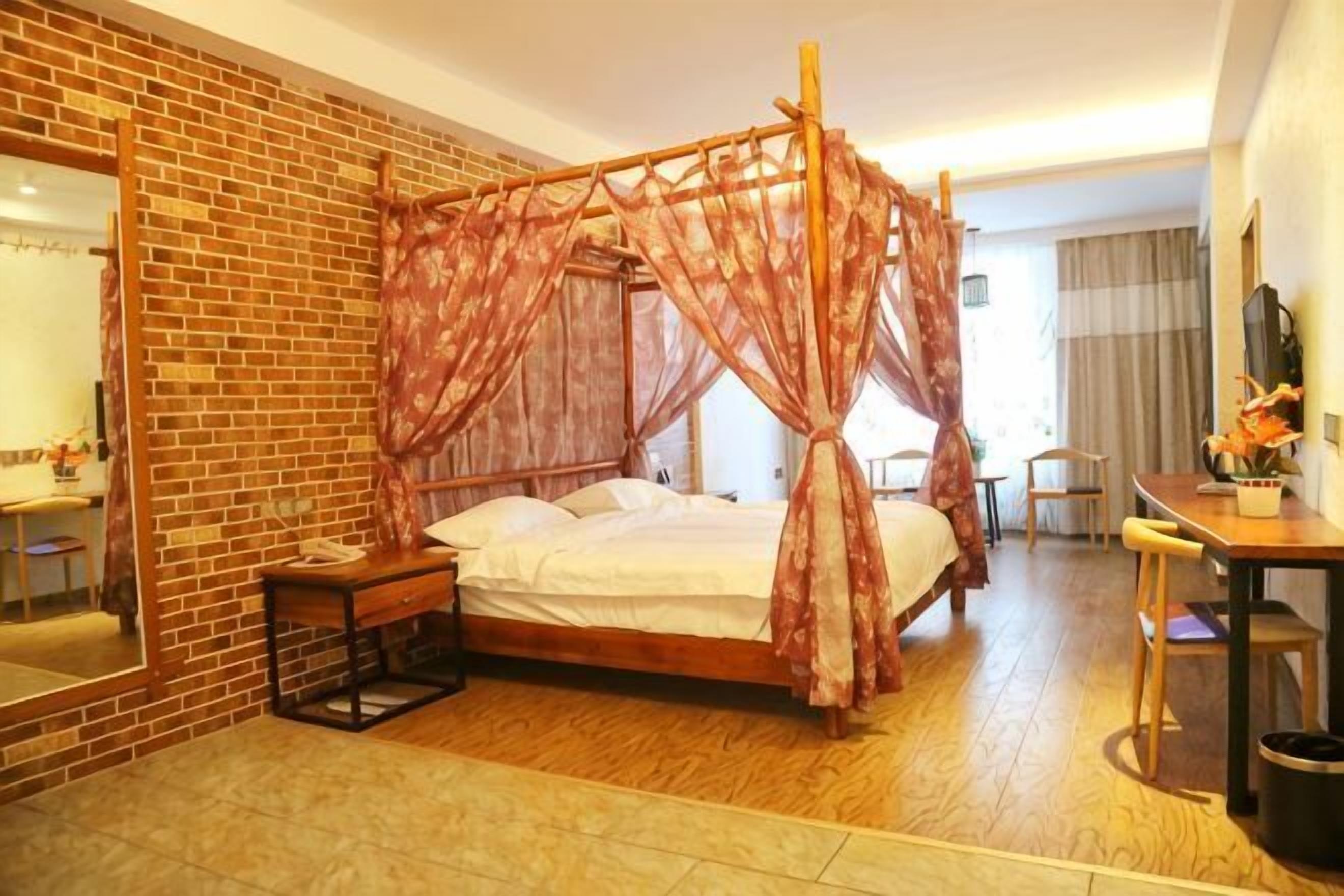 A four-poster bed with a canopy, a wooden desk, a chair, and a small table with a vase of flowers.