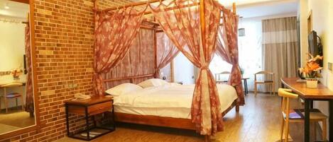 A four-poster bed with a canopy, a wooden desk, a chair, and a small table with a vase of flowers.