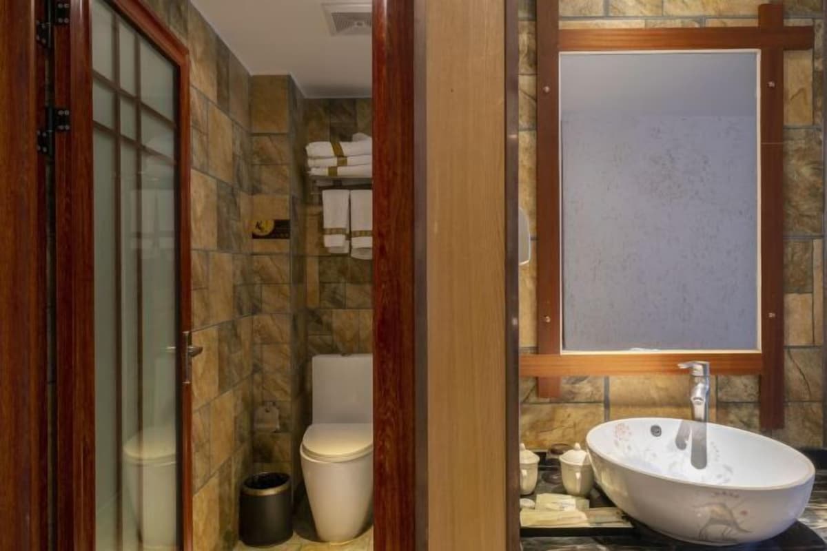 A bathroom with a stone wall, a white toilet, a sink with a mirror, and a towel rack.
